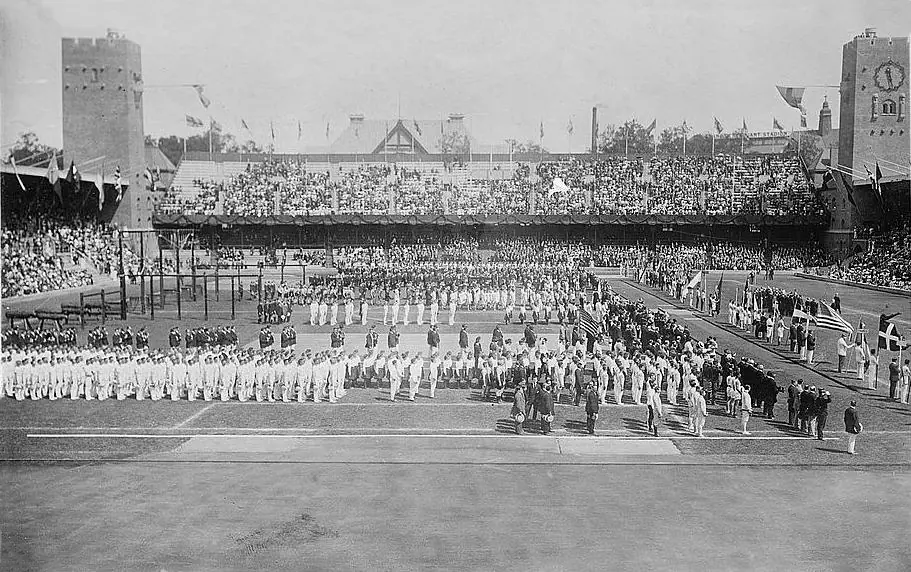 Black-and-white photograph: teams of athletes lined up on the lawn of the Stockholm stadium, in front of packed stands and flags.