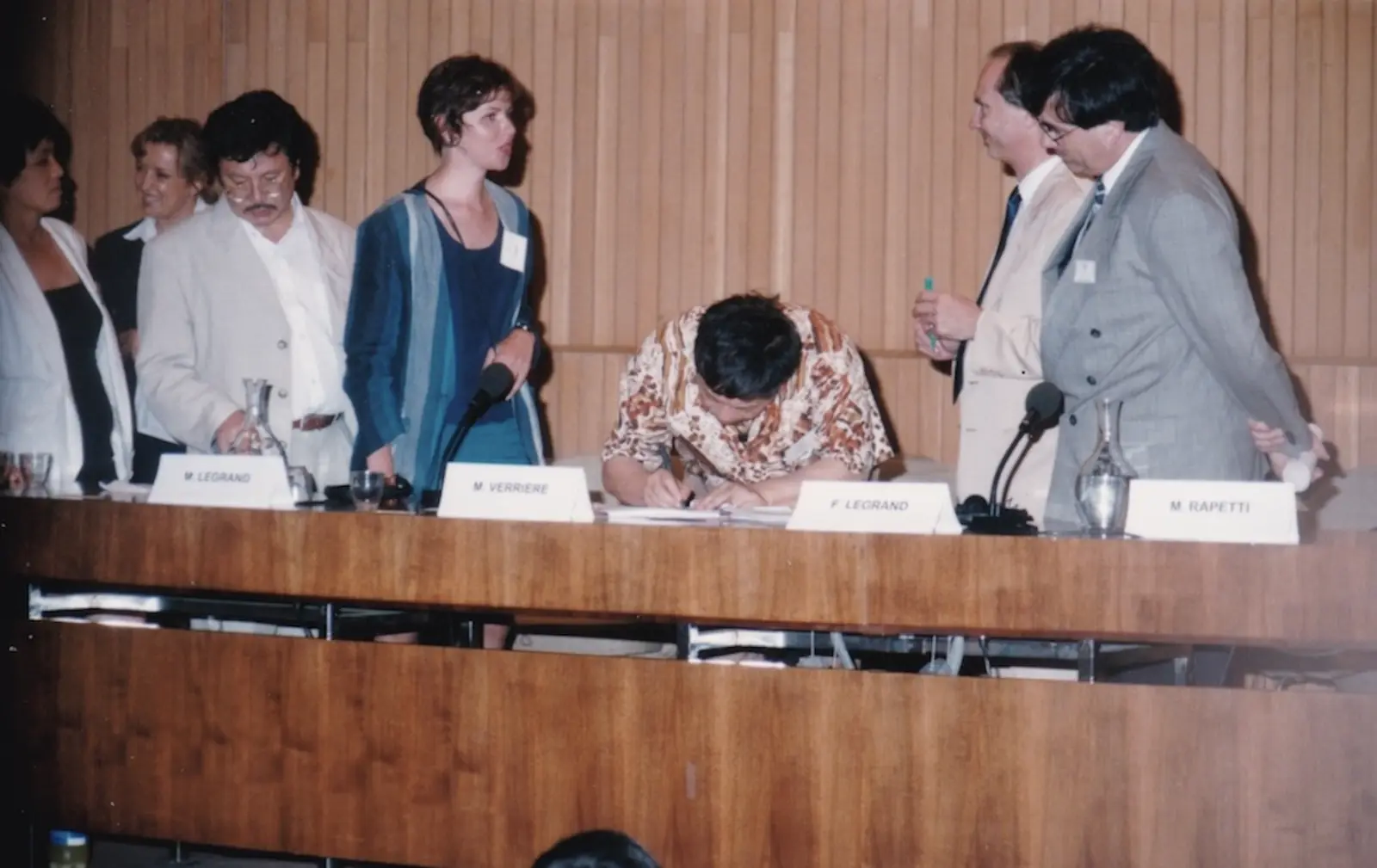 A signatory signs the Charter at the official table, surrounded by standing delegates.