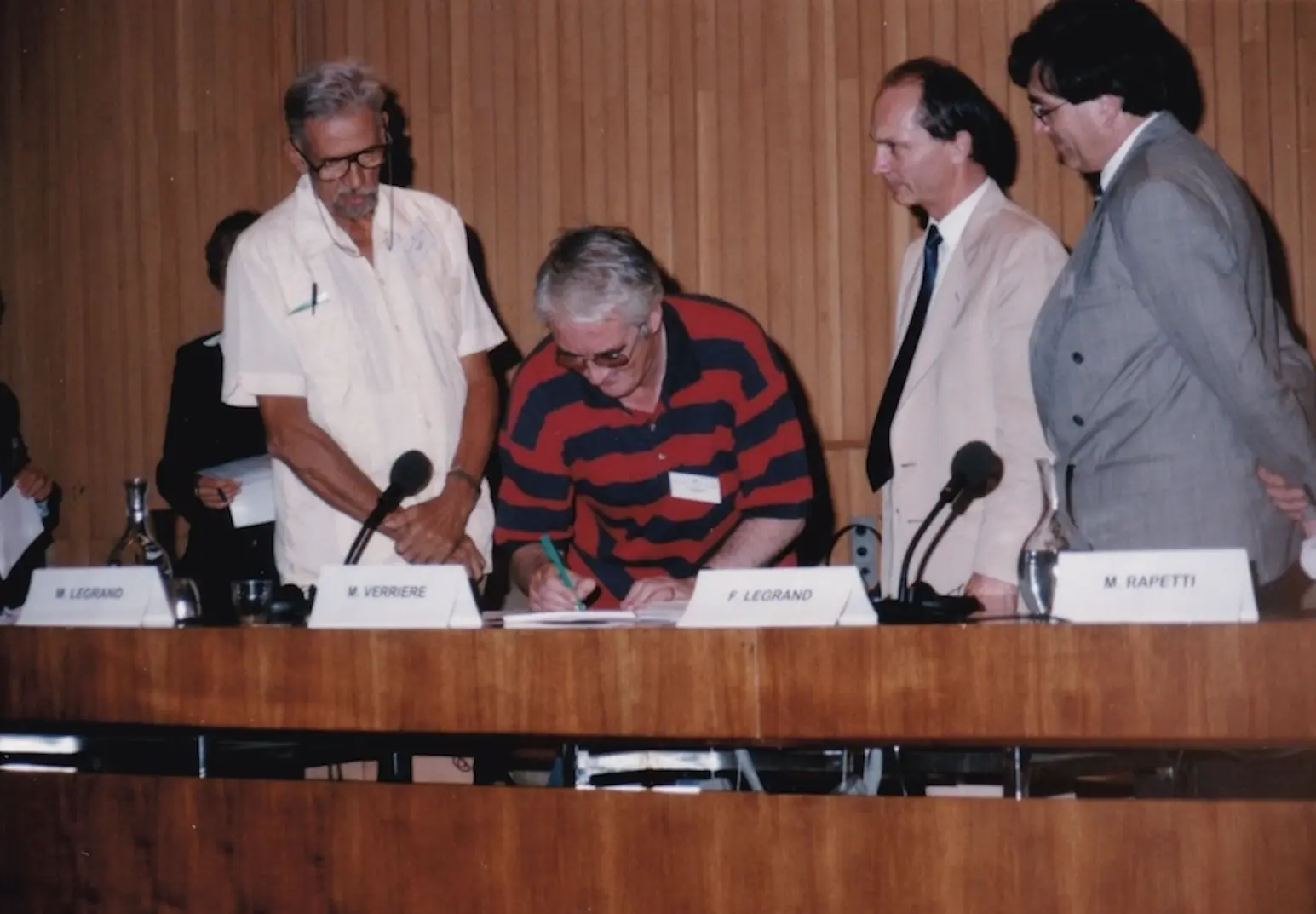A signatory in a striped polo shirt signs the Charter, watched by several delegates.