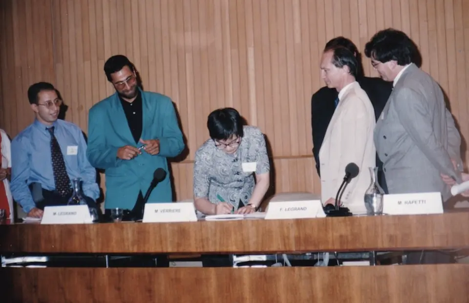 A signatory signs the Charter, surrounded by standing delegates.