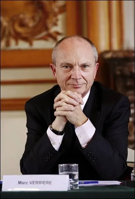 Marc Verrière, hands clasped, at a conference table behind his name card.